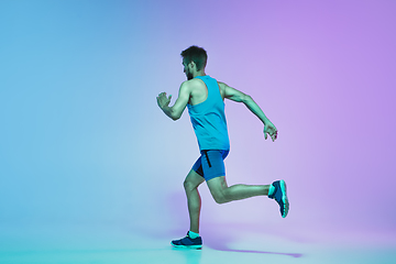 Image showing Full length portrait of active young caucasian running, jogging man on gradient studio background in neon light