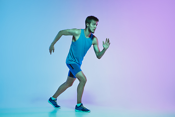 Image showing Full length portrait of active young caucasian running, jogging man on gradient studio background in neon light