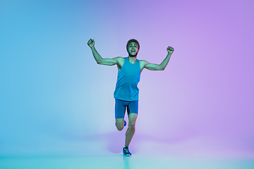 Image showing Full length portrait of active young caucasian running, jogging man on gradient studio background in neon light