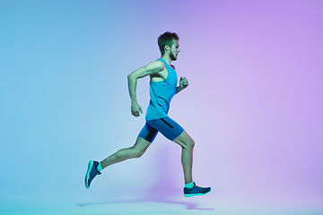 Image showing Full length portrait of active young caucasian running, jogging man on gradient studio background in neon light