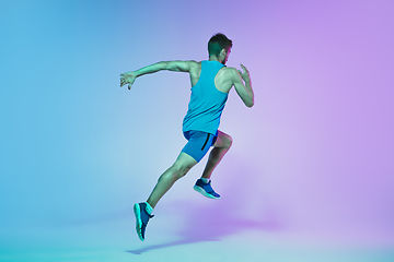 Image showing Full length portrait of active young caucasian running, jogging man on gradient studio background in neon light