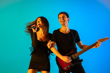 Image showing Caucasian musicians, singer and guitarist, isolated on blue studio background in neon light
