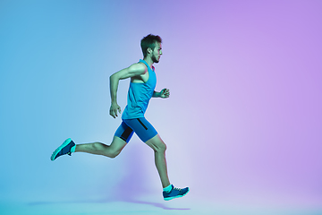 Image showing Full length portrait of active young caucasian running, jogging man on gradient studio background in neon light