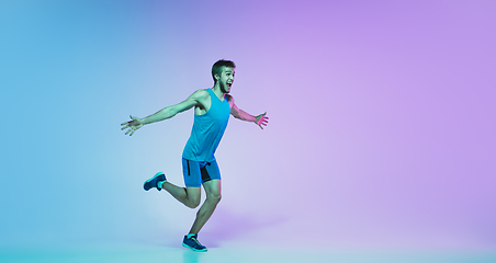 Image showing Full length portrait of active young caucasian running, jogging man on gradient studio background in neon light