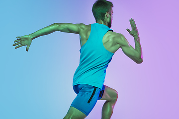 Image showing Full length portrait of active young caucasian running, jogging man on gradient studio background in neon light