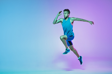 Image showing Full length portrait of active young caucasian running, jogging man on gradient studio background in neon light