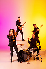 Image showing Young caucasian musicians, band performing in neon light on gradient studio background