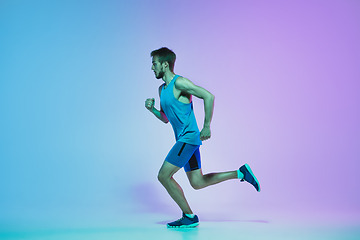 Image showing Full length portrait of active young caucasian running, jogging man on gradient studio background in neon light