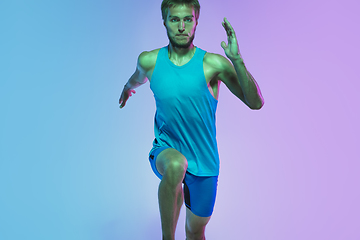 Image showing Full length portrait of active young caucasian running, jogging man on gradient studio background in neon light