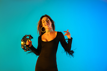 Image showing Caucasian female singer with tambourin isolated on blue studio background in neon light