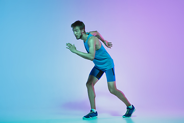 Image showing Full length portrait of active young caucasian running, jogging man on gradient studio background in neon light