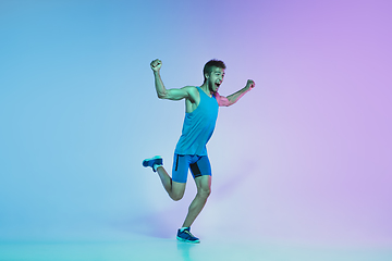 Image showing Full length portrait of active young caucasian running, jogging man on gradient studio background in neon light