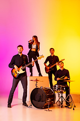 Image showing Young caucasian musicians, band performing in neon light on gradient studio background