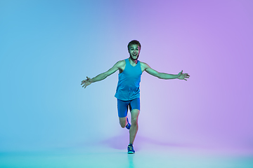 Image showing Full length portrait of active young caucasian running, jogging man on gradient studio background in neon light