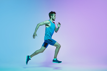 Image showing Full length portrait of active young caucasian running, jogging man on gradient studio background in neon light