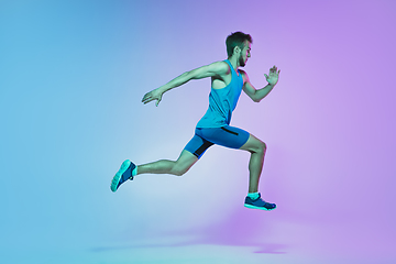 Image showing Full length portrait of active young caucasian running, jogging man on gradient studio background in neon light