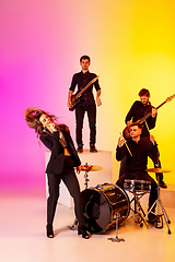 Image showing Young caucasian musicians, band performing in neon light on gradient studio background