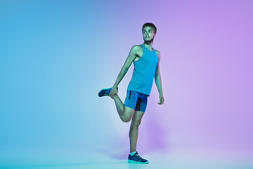 Image showing Full length portrait of active young caucasian running, jogging man on gradient studio background in neon light