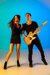 Image showing Caucasian musicians, singer and guitarist, isolated on blue studio background in neon light