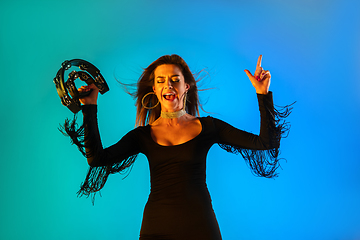 Image showing Caucasian female singer with tambourin isolated on blue studio background in neon light