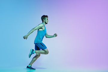 Image showing Full length portrait of active young caucasian running, jogging man on gradient studio background in neon light