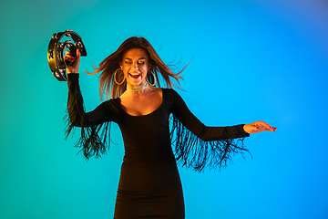 Image showing Caucasian female singer with tambourin isolated on blue studio background in neon light