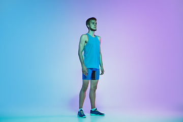 Image showing Full length portrait of active young caucasian running, jogging man on gradient studio background in neon light