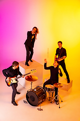 Image showing Young caucasian musicians, band performing in neon light on gradient studio background