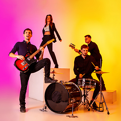 Image showing Young caucasian musicians, band performing in neon light on gradient studio background