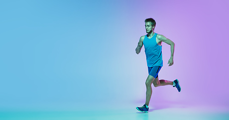 Image showing Full length portrait of active young caucasian running, jogging man on gradient studio background in neon light