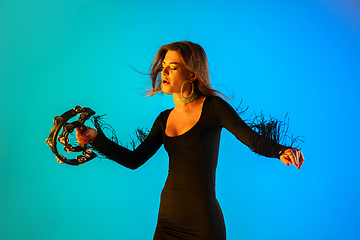 Image showing Caucasian female singer with tambourin isolated on blue studio background in neon light