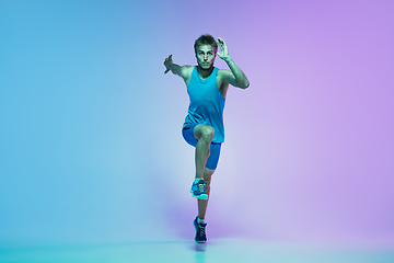 Image showing Full length portrait of active young caucasian running, jogging man on gradient studio background in neon light