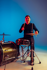 Image showing Caucasian male drummer improvising isolated on blue studio background in neon light