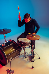 Image showing Caucasian male drummer improvising isolated on blue studio background in neon light