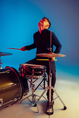 Image showing Caucasian male drummer improvising isolated on blue studio background in neon light