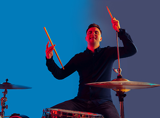 Image showing Caucasian male drummer improvising isolated on blue studio background in neon light