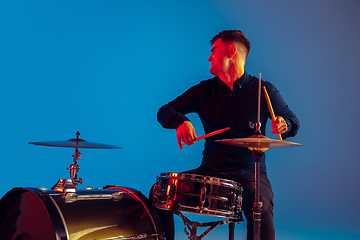 Image showing Caucasian male drummer improvising isolated on blue studio background in neon light