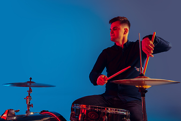 Image showing Caucasian male drummer improvising isolated on blue studio background in neon light