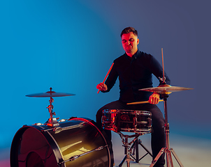 Image showing Caucasian male drummer improvising isolated on blue studio background in neon light