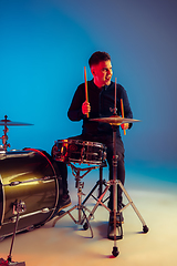 Image showing Caucasian male drummer improvising isolated on blue studio background in neon light