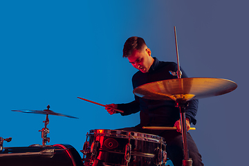 Image showing Caucasian male drummer improvising isolated on blue studio background in neon light