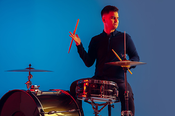 Image showing Caucasian male drummer improvising isolated on blue studio background in neon light