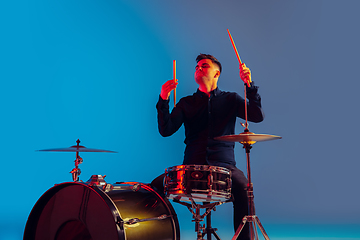 Image showing Caucasian male drummer improvising isolated on blue studio background in neon light