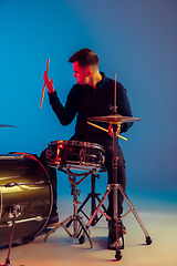 Image showing Caucasian male drummer improvising isolated on blue studio background in neon light