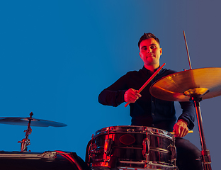 Image showing Caucasian male drummer improvising isolated on blue studio background in neon light