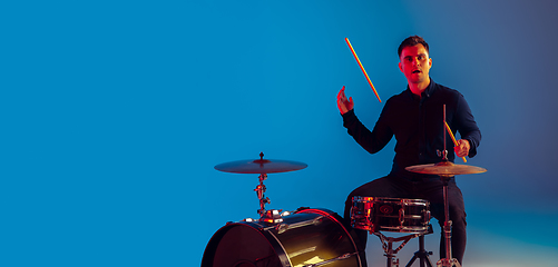 Image showing Caucasian male drummer improvising isolated on blue studio background in neon light