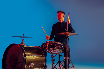 Image showing Caucasian male drummer improvising isolated on blue studio background in neon light