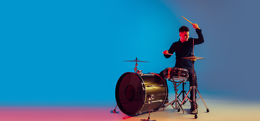 Image showing Caucasian male drummer improvising isolated on blue studio background in neon light