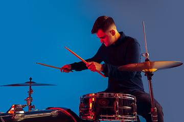 Image showing Caucasian male drummer improvising isolated on blue studio background in neon light