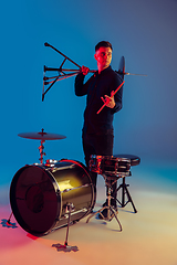 Image showing Caucasian male drummer improvising isolated on blue studio background in neon light